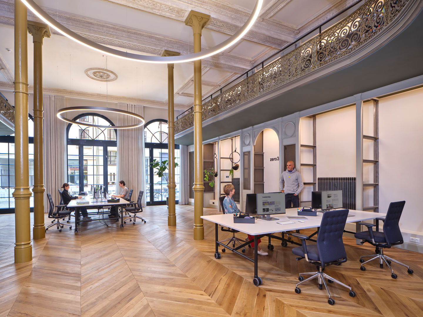 Open space aménagé par Jbonet avec colonnes dorées, bureaux partagés et suspensions circulaires